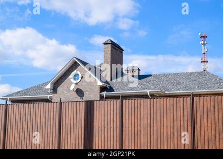 Asphalt Kies. Dekorative bitumen Schindeln auf dem Dach eines Brick House. Zaun aus Wellblech Stockfoto