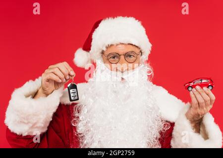 Santa claus in Brillen mit Automodell und Schlüssel isoliert auf rot Stockfoto