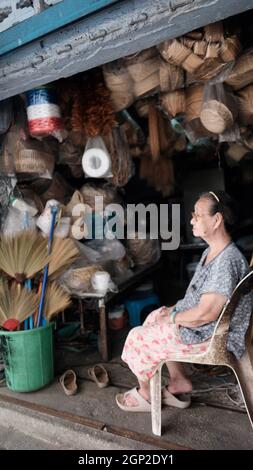 Die alte Dame sitzt auf einem Stuhl vor ihrem Basket Shop Bangkok Thailand Stockfoto