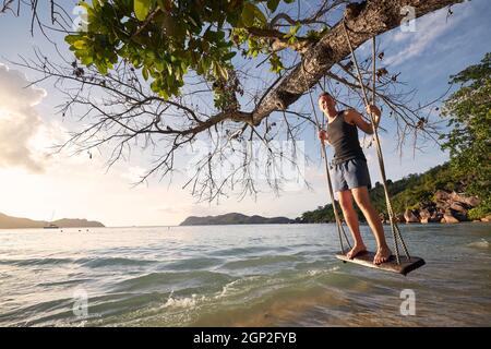 Schöner sonniger Tag am Strand. Glücklicher Mann auf Schaukel, der den Urlaub auf den Seychellen genießt. Stockfoto