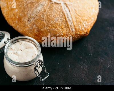 Sauerteig Vorspeise und Weizensauerteig Brot. Weizen sauren Teig Starter im Glas und köstliche hausgemachte runde Sauerteig Brot auf schwarzem Hintergrund, CO Stockfoto