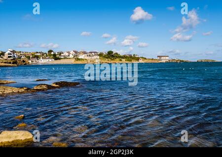 Blick über das Meer auf die Küste des Dorfes mit Rettungsbootstation und Insel. Moelfre, Isle of Anglesey, Nordwales, Großbritannien, Europa Stockfoto