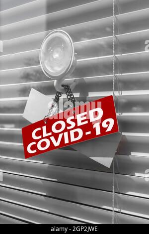 Nahaufnahme auf einem roten geschlossenen Schild im Fenster eines Geschäfts/Büros mit der Meldung „Geschlossen wegen Covid-19“. Stockfoto