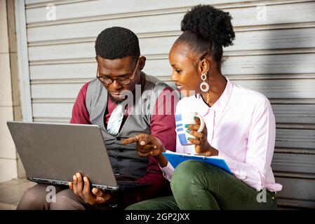 afrikanisches Geschäftsehepaar sitzt zusammen, Frau zeigt mit dem Finger auf den Computerbildschirm, um ihrem Chef etwas zu zeigen Stockfoto