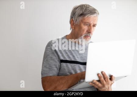 Ein älterer Mann, der zu Hause einen Laptop benutzt, ein bisschen mit der Technologie zu kämpfen hat, während der COVID-Sperre/Quarantäne online einkaufen Stockfoto