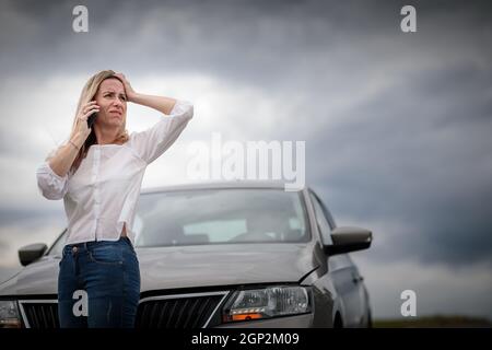 Ziemlich Frau mittleren Alters, die Autoprobleme hat - zusammengebrochenes Auto auf der Seite der Straße, die Versicherungsgesellschaft um Hilfe zu rufen Stockfoto