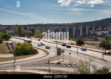 Blick auf das historische Aqueduto das Águas Livres, das sich über das Tal in Lissabon erstreckt, mit einer modernen Straße im Vordergrund. Stockfoto