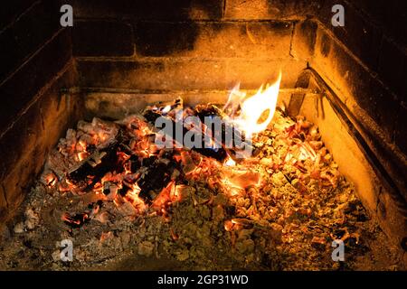 Schwelendes Feuerholz und heiße Asche im Kamin Stockfoto