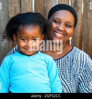 Porträt von afrikanischer Mutter und Tochter gegen Holzzaun. Stockfoto