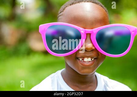 Nahaufnahme Porträt des niedlichen afrikanischen Jungen trägt riesige übergroße Sonnenbrille im Freien. Stockfoto