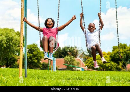 Actionportrait schreiender afrikanischer Kinder, die in der Nachbarschaft auf Schaukel spielen.außer Fokus geratenen Häuser im Hintergrund. Stockfoto