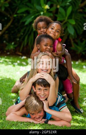 Multirassische Kinder spielen zusammen und bilden im Garten einen Menschenhaufen. Stockfoto