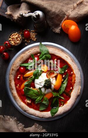 Pizza mit Burrata-Käse und Pinienkernen. Italienische Pizza. Metallplatte zum Servieren. Grüne Basilikumblätter. Vertikales Foto. Draufsicht. Stockfoto
