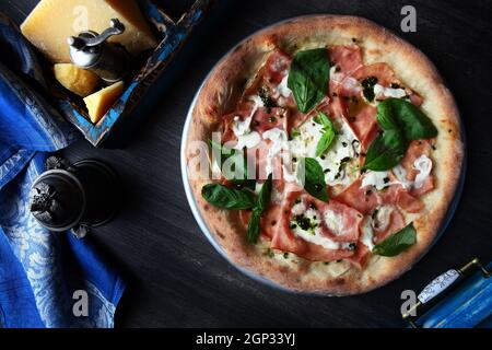 Pizza mit Schinken. Traditionelle italienische Pizza. Metallplatte zum Servieren von Pizza. Ein Stück Parmesan. Blaue Baumwollserviette. Draufsicht. Stockfoto
