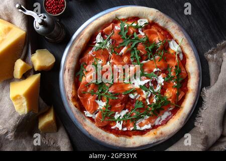 Pizza mit rotem Flussfisch. Traditionelle italienische Pizza. Metallplatte zum Servieren. Ein Stück Parmesan und rote Pfefferkörner. Draufsicht. Stockfoto