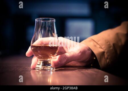 Nahaufnahme einer Hand, die ein Glencairn Whisky-Glas auf einem Holztisch hält, mit geringer Schärfentiefe. Stockfoto