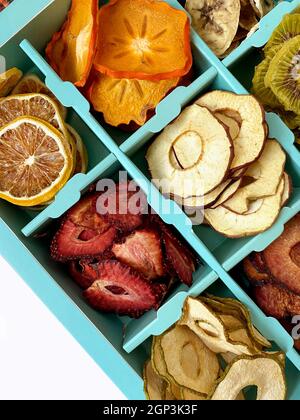 Box mit getrockneten Früchten Chips isoliert auf weiß, Draufsicht. Ananas, Kokosnuss, Kiwi, Erdbeere, Orange, Birne, Apfel, Banane natürliche Chips Stockfoto