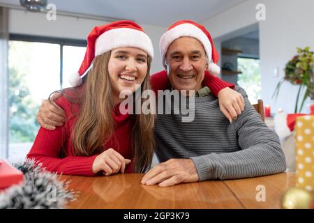 Kaukasische Frau und älterer Mann mit weihnachtsmann-Hüten, die zur weihnachtszeit einen Videoanruf führen Stockfoto