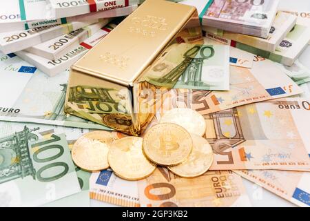 Bitcoin BTC Goldmünzen mit Rechnungen von Euro-Banknoten und Gold Bullion. Bitcoin und Gold liegen auf Euro-banknoten Stockfoto