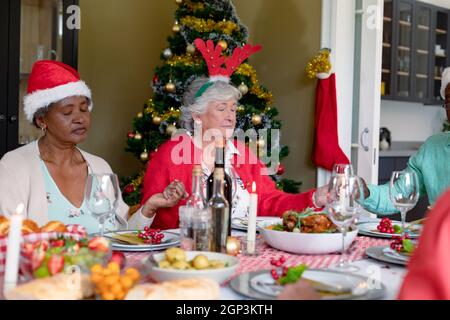 Eine vielfältige Gruppe glücklicher älterer Freunde betet und feiert weihnachten zu Hause Stockfoto