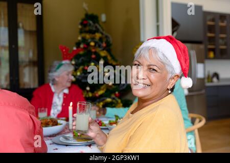 Glückliche gemischte Rennen Senior Frau hält Glas und feiert weihnachten mit verschiedenen Gruppe von Freunden Stockfoto