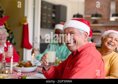 Glücklicher kaukasischer älterer Mann, der Glas hält und Weihnachten mit verschiedenen Freunden feiert Stockfoto
