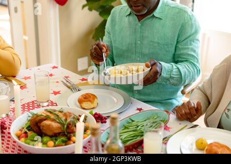 Mittelteil eines afroamerikanischen Senioren, der eine Schüssel hält und Weihnachten mit einer Gruppe von Freunden feiert Stockfoto