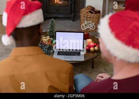 Rückansicht von verschiedenen Männern in weihnachtsmännern, die zur weihnachtszeit einen Laptop mit Platz zum Kopieren auf dem Bildschirm verwenden Stockfoto