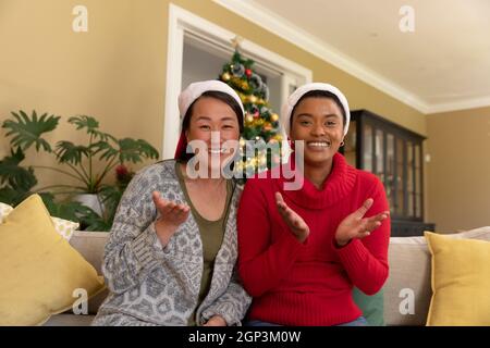 Zwei glückliche, vielfältige Freundinnen in Weihnachtsmützen, die zur weihnachtszeit einen Videoanruf führen Stockfoto