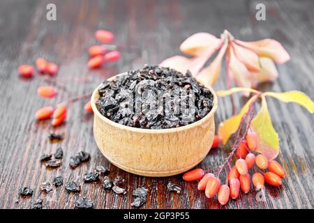 Getrocknete schwarze Berberitze in einer Schüssel, Zweige mit frischen Beeren und Blätter auf Holzbrett Hintergrund Stockfoto