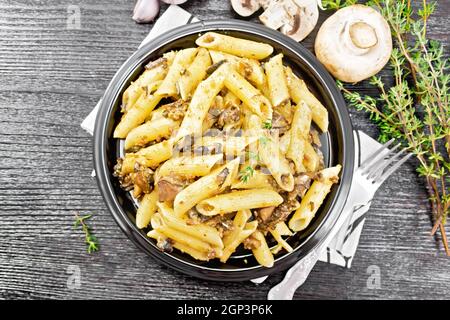 Penne Pasta mit Pilzen in einem Teller auf einem Handtuch, Thymian, Gabel und Knoblauch auf Holzbrett Hintergrund von oben Stockfoto