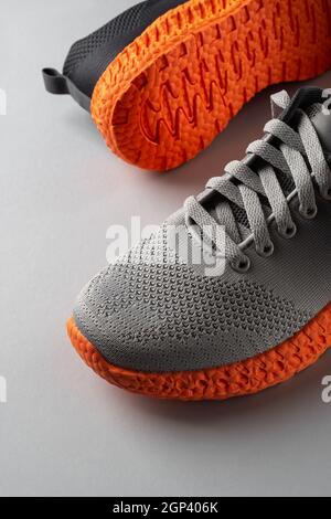 Gerillte, orange Sohle-Sneakers mit grauen elastischen Schnürsenkeln auf grauem Hintergrund. Zwei neue Turnschuhe aus Mesh-Material für aktiven Lifestyle und Fitness. Nahaufnahme Stockfoto