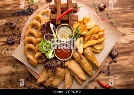 Gebratener Snack für Bier. Großer Teller mit Biersnacks: Croutons, gebratene Zwiebelringe im Teig, pommes Frites, Kartoffelkeile. Heiße Sauce und Käsesauce für s Stockfoto