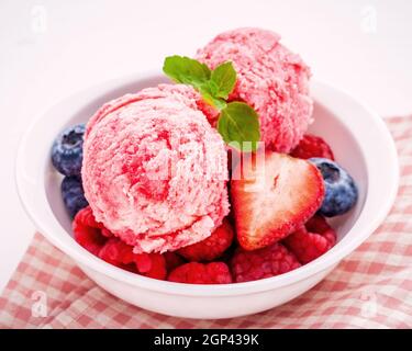 Close Up Eis mixed berry Früchte Himbeere, Heidelbeere, Erdbeere und Pfefferminze Blätter setup in Weiß Schüssel auf weißem Holz- Hintergrund. Sommer ein Stockfoto