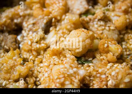 Detail der Zutaten einer Reispaella mit Blumenkohl und halbgekochten Schweinefleischrippen. Typischer valencianischer Reis Stockfoto