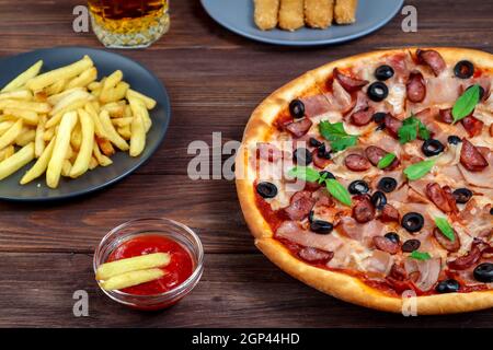 Pizza auf einer Platte Nahaufnahme auf dem Tisch mit Ketchup, Saft, Sauce und Kartoffeln auf einem dunklen Holztisch im rustikalen Stil. Stockfoto