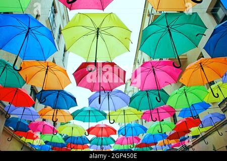 Farbige Regenschirme hängen oben. Set von verschiedenen Regenschirmen. Lokales Wahrzeichen Stockfoto