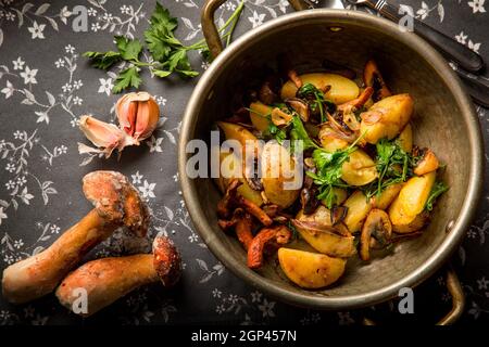 Gebratene Kartoffeln im Landhausstil mit Zwiebeln und geschmorten Pilzen und Kräutern. Servierbesteck: Besteck und Einrichtung. Konzept: Speisekarte für ein Restaurant. Stockfoto