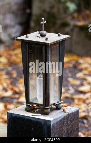 Laterne aus Metall mit Glasfenstern auf einem Steinsockel Vor einem verschwommenen Hintergrund mit Herbstblättern Stockfoto