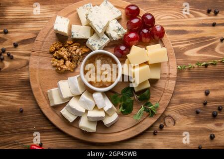 Vorspeise mit verschiedenen Käsesorten für Wein. Käseplatte sortiert: dor blau, Cheddar, Ziegenkäse, Feta-Käse. Nüsse und Honig für Käse. Konzept - Männer Stockfoto