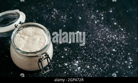 Weizensauerteig-Starter. Glasgefäß mit Sauerteig Starter auf dunklem Hintergrund, Kopierraum. Stockfoto