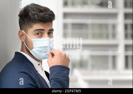 Porträt eines gutaussehenden Mannes in medizinischer Maske, der die Stadt vor die Kamera schaut. Hübscher junger Mann, der im Freien in einer medizinischen Maske steht. Coronavirus-Konzept. Hochwertige Fotos Stockfoto