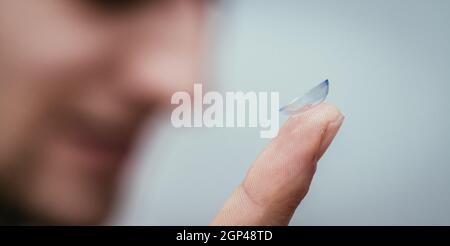 In der Nähe Bild von Kontaktlinsen auf einem mans Finger. Gesicht in der verschwommenen Hintergrund. Stockfoto