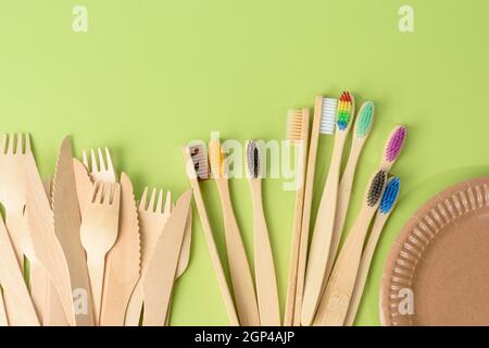 Zahnbürsten und Holzgabel und leere runde braune Einwegplatte aus recycelten Materialien auf grünem Hintergrund, Draufsicht. Konzept der absen Stockfoto
