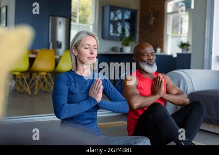 Glückliches, vielseitiges Paar in Übungskleidung, das gemeinsam Yoga praktiziert und meditiert Stockfoto