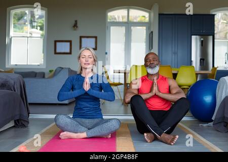 Glückliches, vielseitiges Paar in Übungskleidung, das gemeinsam Yoga praktiziert und meditiert Stockfoto