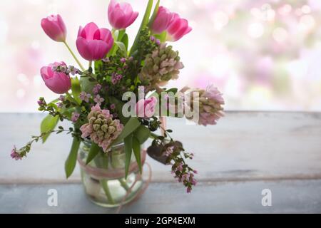 Komposition mit frischen Frühlingsblumen auf grauem Holz, im Hintergrund zartes romantisches rosa Bokeh mit Platz für Text. Kurze Schärfentiefe Stockfoto