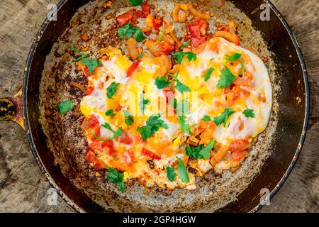 Gebratenes Omelett mit Eiern im Landhausstil mit Tomaten und Zwiebeln. Alte Bratpfanne mit Eiern auf Holzboden. Konzept - fetthaltige Lebensmittel, Adipositas Stockfoto