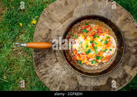 Gebratenes Omelett mit Eiern im Landhausstil mit Tomaten und Zwiebeln. Alte Bratpfanne mit Eiern auf Holzboden. Konzept - fetthaltige Lebensmittel, Adipositas Stockfoto