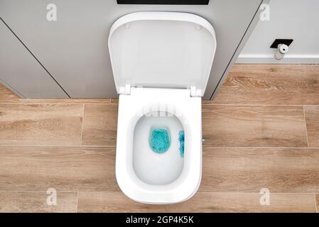 Eine weiße Keramik-Toilette mit offener Klappe in einem modernen Badezimmer, ein Boden mit Keramikfliesen, die Holz imitieren, Draufsicht. Stockfoto